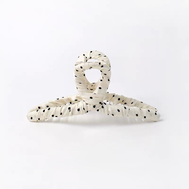 An off-white crinkled hair claw clip with black polka dots, photographed on a seamless white background.