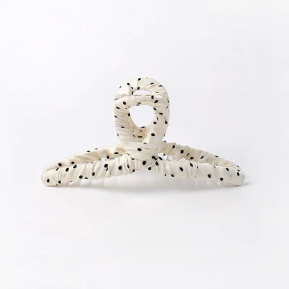An off-white crinkled hair claw clip with black polka dots, photographed on a seamless white background.